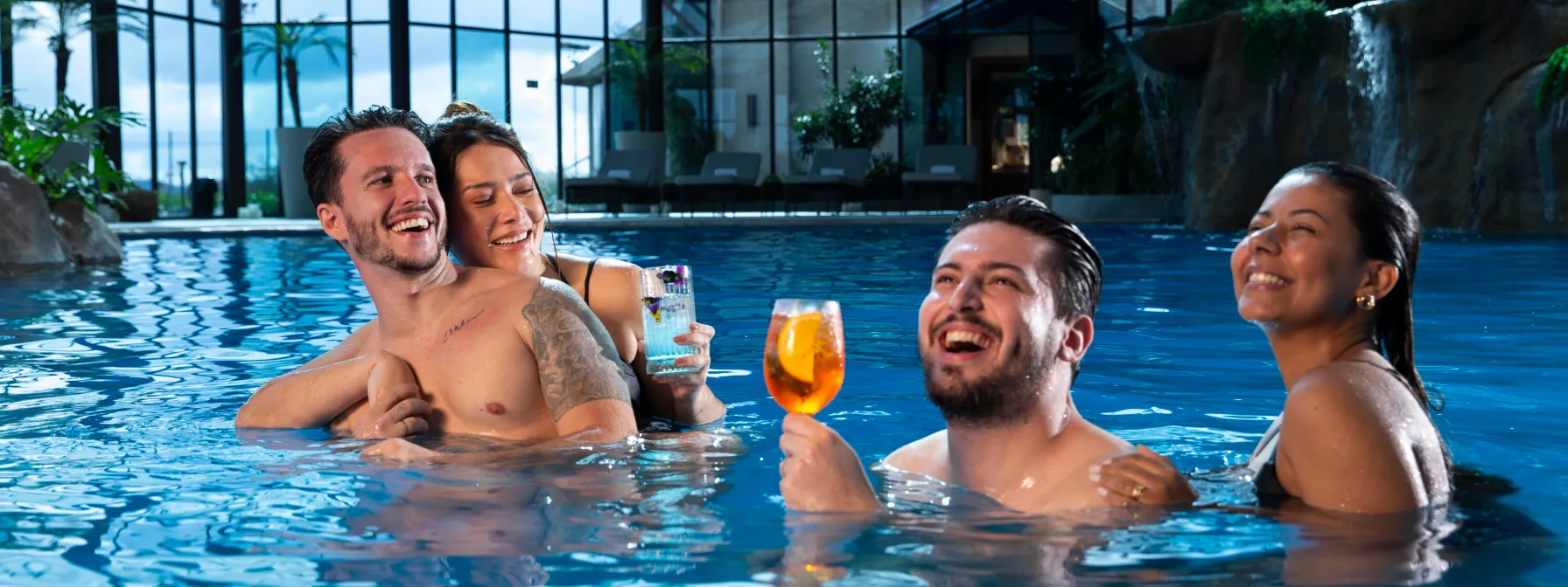 Um grupo de pessoas está em uma piscina segurando bebidas.
