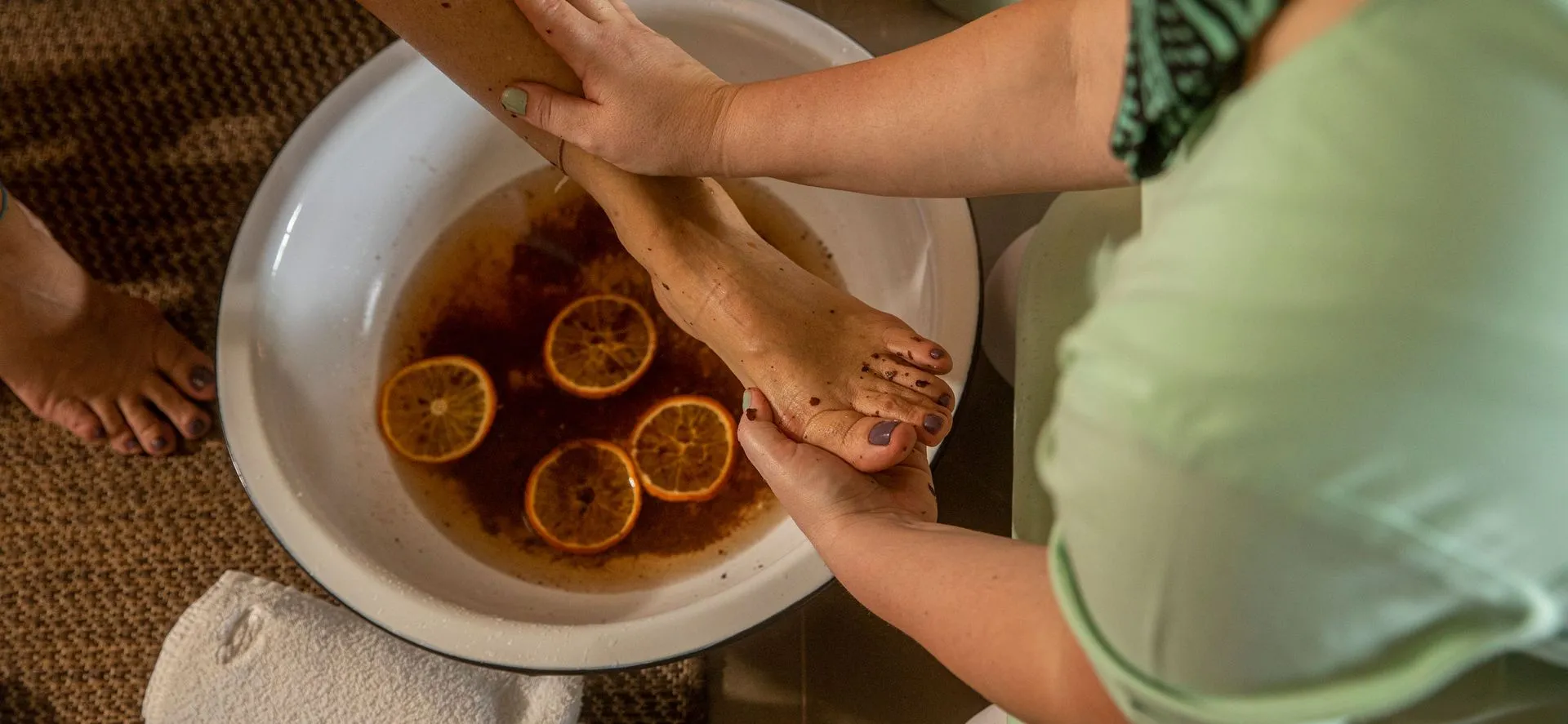 Uma mulher está lavando os pés de uma pessoa em uma tigela de água com rodelas de limão.