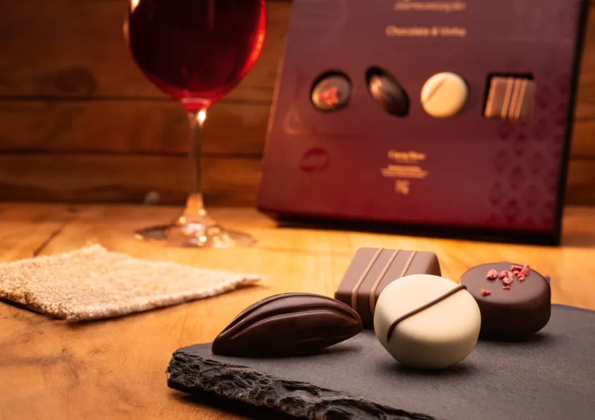 Uma caixa de chocolates está sobre uma mesa ao lado de uma taça de vinho.
