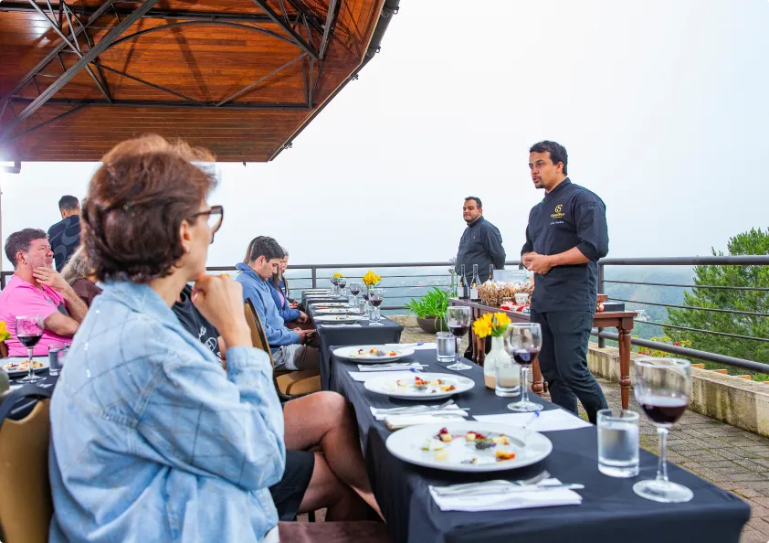 Um grupo de pessoas está sentado à mesa com pratos de comida e taças de vinho.